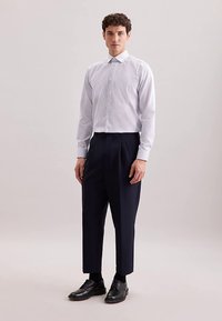 Camicia a righe bianche con colletto appuntito, abbinata a pantaloni plissettati blu navy scuro e scarpe eleganti nere, con una vestibilità su misura.