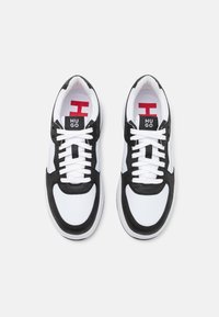 Svart-vita sneakers med en slät läder- och mocka-finish, snörning, med en röd logotyp på tungan och en gummisula.