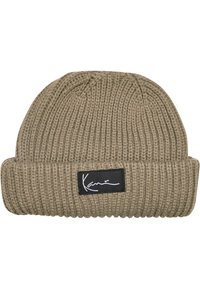 Beanie i olivengrønn, ribbet strikketekstur, med et svart stoffmerke med hvit signatur. Brettet mansjett for justerbar passform.