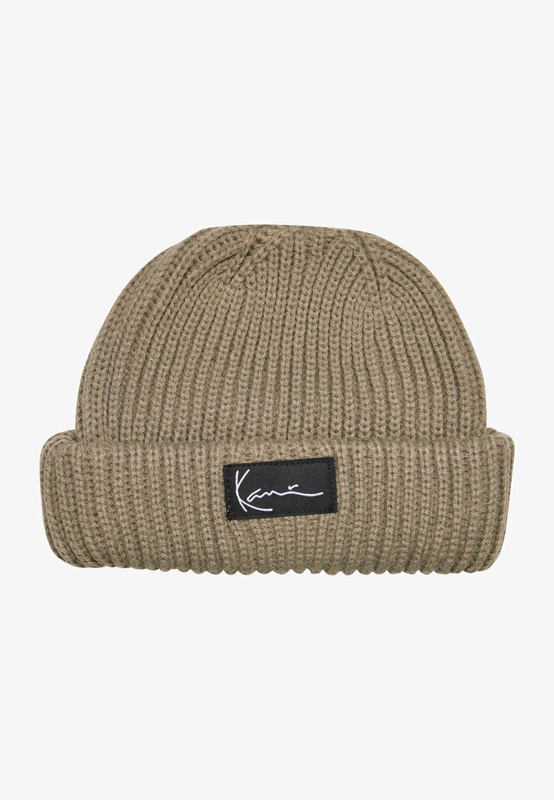 Beanie hat in olive green, ribbed knit texture, featuring a black fabric patch with white signature. Folded cuff for adjustable fit.