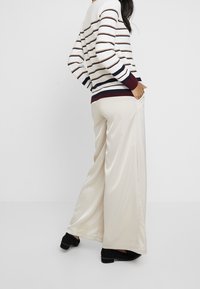 Kremowe szerokie spodnie wykonane z materiału przypominającego satynę, w połączeniu z paskowaną bluzą w kolorze bordowym, granatowym i beżowym.