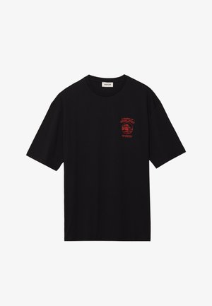 T-shirt en coton noir à manches courtes et coupe décontractée. Il présente un imprimé graphique rouge sur la poitrine avec l'inscription "UN VOYAGE DE RÉVÉLATION".