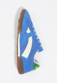 Modri semiš in platneni adidas z belimi detajli, strukturiranimi vezalkami, zelenim petnim trakom in rjavim gumijastim podplatom. Nizkoprofesionalna zasnova.