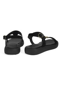 Schwarze Wildleder-Sandalen mit verstellbarem Riemen und goldenen Beschlägen. Flache Sohle mit glatter Textur und minimalistischem Design. Robuste Verarbeitung.