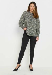 Blus med blommönster i mörkgrön och krämfärgad, med långa ärmar, knäppning i halsen och avslappnad passform, matchad med svarta smala jeans och klackskor.