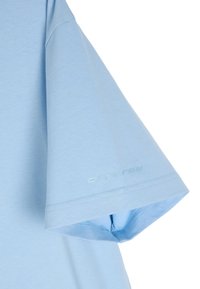 Jasnoniebieska bawełniana koszulka z krótkim rękawem. Posiada subtelne logo nadrukowane na rękawie oraz gładką, jednolitą teksturę.