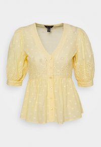 Gelbe Bluse mit V-Ausschnitt, Puffärmeln und Knopfverschluss. Hergestellt aus leichtem Stoff mit Lochstickerei und ausgestelltem Saum.