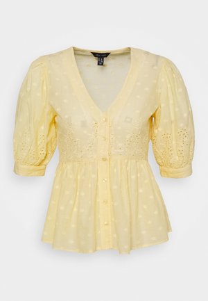 Žlutá halenka s výstřihem do V, nabíranými rukávy a zapínáním na knoflíky. Vyrobena z lehké látky s výšivkou očkování a rozšířeným lemem.