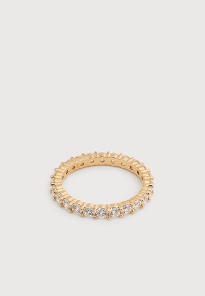 Bague éternité en or avec des diamants ronds taillés uniformément espacés tout autour de l'anneau sur un fond clair uni.