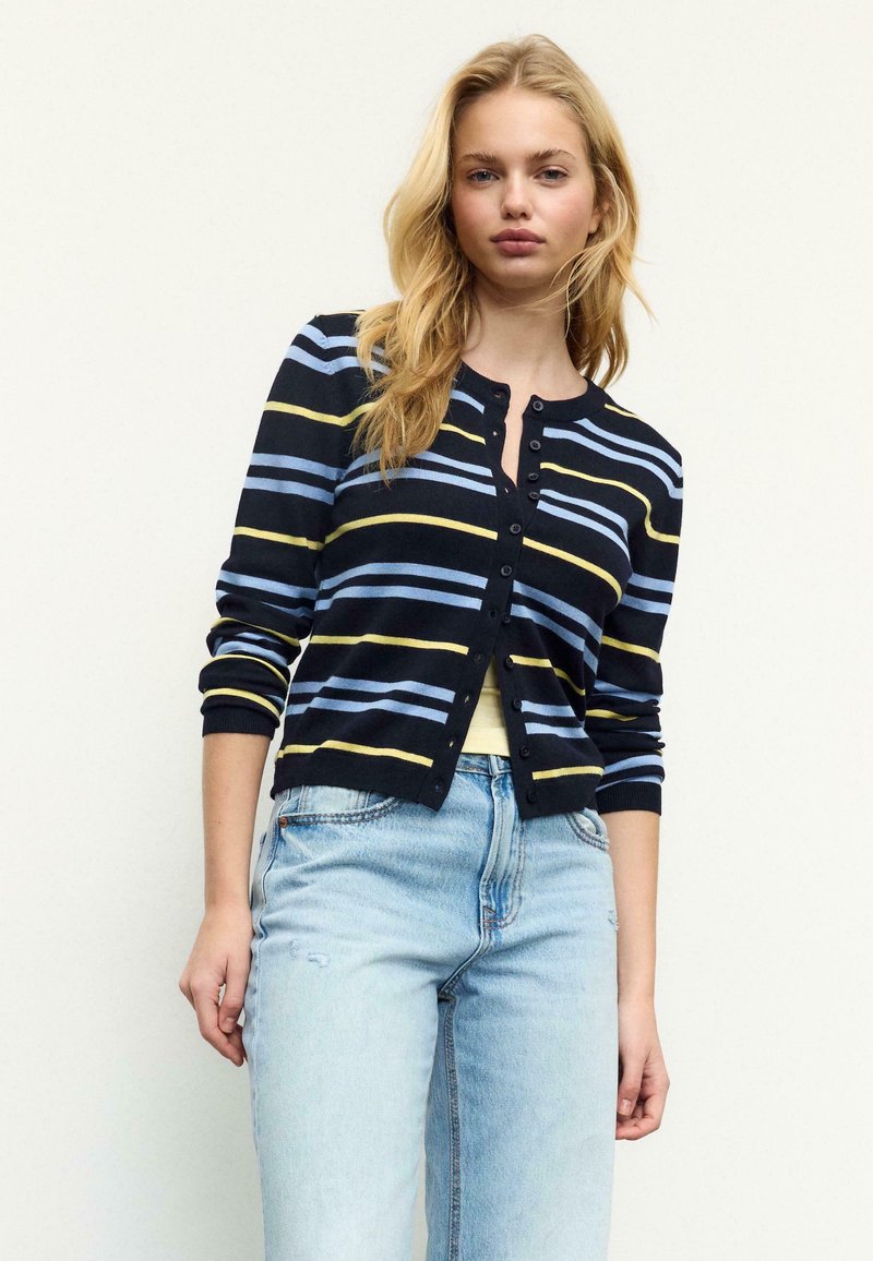 Cardigan bleu marine avec des rayures horizontales en bleu clair et jaune. Il présente un col rond, une fermeture à six boutons et des manches longues.
