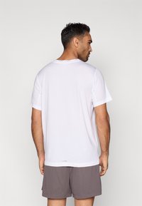 Hvid t-shirt med korte ærmer og rund halsudskæring, glat tekstur og afslappet pasform, kombineret med grå træningsshorts.