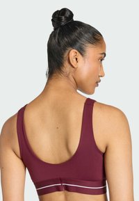 Burgundy sports bra in a fitted design with a wide band featuring a white stripe, smooth texture, and rounded back.