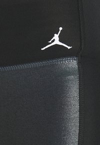 Logo Jumpman blanc sur tissu noir avec coutures visibles et panneau texturé brillant d’un côté.