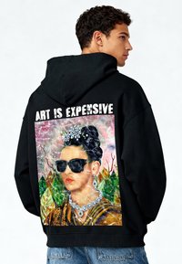 Felpa nera con cappuccio con una grande grafica di una donna con occhiali da sole sul retro, circondata da motivi colorati e testo che recita "L'ARTE È COSTOSA."