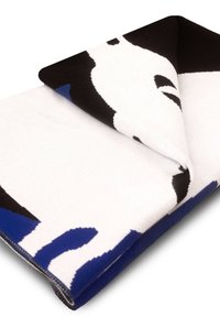 Koc dziergany z wyrazistymi abstrakcyjnymi wzorami w czerni, bieli i niebieskim; miękka tekstura z zagiętymi brzegami, podkreślająca żywy kontrast kolorów.