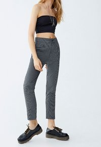 Černý top bez ramínek, šedé kalhoty se vzorem, slim fit a ke kotníkům. Obuv: černé boty s hrubou podrážkou a krajkami.