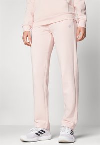 Calças de treino cor-de-rosa claro feitas de um tecido macio, com ajuste slim, cintura elástica e um pequeno logótipo tonal na frente.