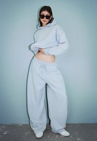 Light gray oversized hoodie with a kangaroo pocket and matching wide-leg sweatpants. Smooth texture, casual fit, worn with white shoes.