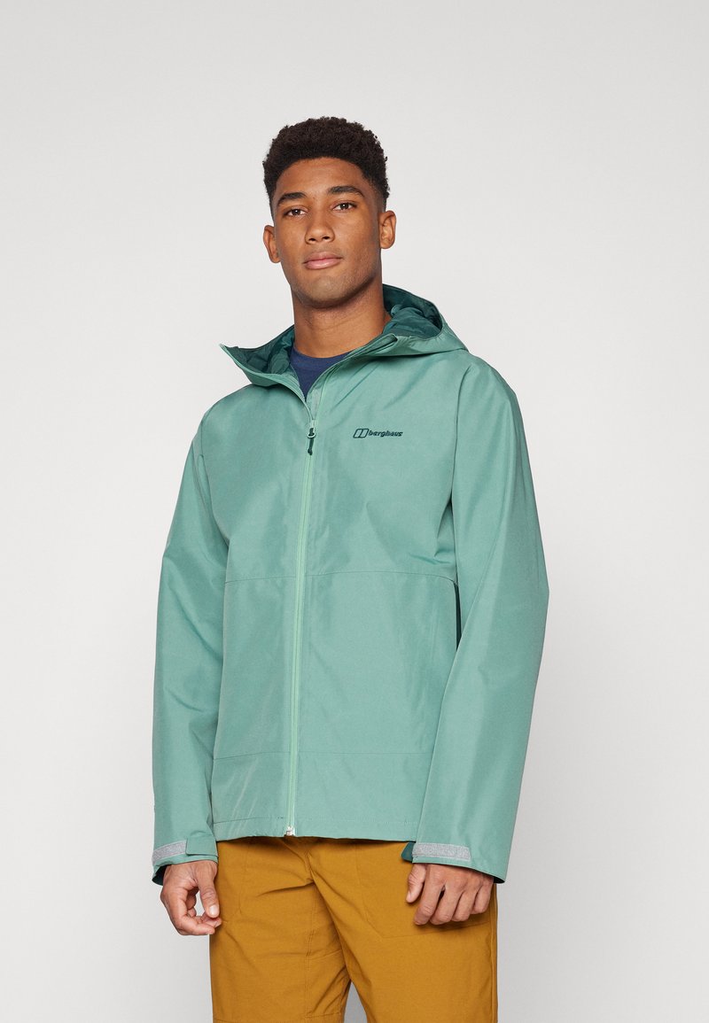 Chaqueta impermeable de color verde claro, fabricada en material sintético, con cremallera frontal, capucha ajustable y puños elásticos. Presenta un logo en el pecho.