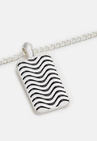 Pendente de prata em forma retangular com um padrão ondulado em preto. Afixado a uma delicada corrente de prata. Textura suave.