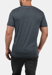 Graues Kurzarm-T-Shirt aus einem weichen, strukturierten Stoff mit Rundhalsausschnitt, das einen dezenten Druck im oberen Rückenbereich aufweist.