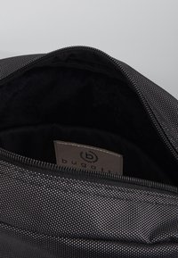 Schwarzer, strukturierter Innenraum der Tasche mit glattem, schwarzem Futter und einem sichtbaren Etikett mit dem Markennamen "bugatti". Mit Reißverschluss.