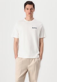 Witte katoenen t-shirt met een klein blauw geborduurd logo op de linkerborst. Het shirt heeft een relaxte pasvorm en korte mouwen.