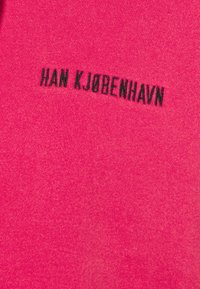 Tissu rose vif avec le texte "HAN KJØBENHAVN" brodé en noir centré sur la surface.