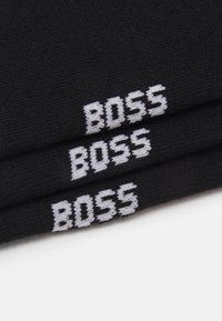 Čierne ponožky s bielym nápisom "BOSS" pleteným na manžete, s jemnou textúrou a klasickým dizajnom.