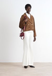 Brown double-breasted jacket, white shirt, and white flared trousers. Black pointed-toe heels and a small burgundy handbag complete the look.