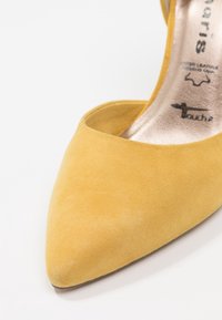 Décolleté in camoscio giallo con punta affilata, caratterizzata da un interno metallico liscio. Il design include un'apertura bassa e nessuna ferramenta visibile.