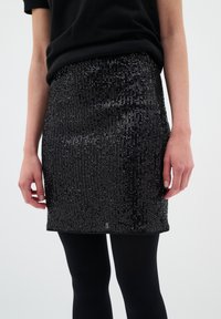 Mini jupe noire à sequins avec un design ajusté. La texture présente des rangées horizontales de sequins brillants, créant un effet scintillant.
