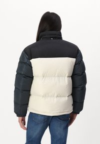 Chaqueta acolchada con parte superior negra, medio crema y mangas en verde oscuro. Presenta puños acanalados, un cuello alto y una silueta amplia.