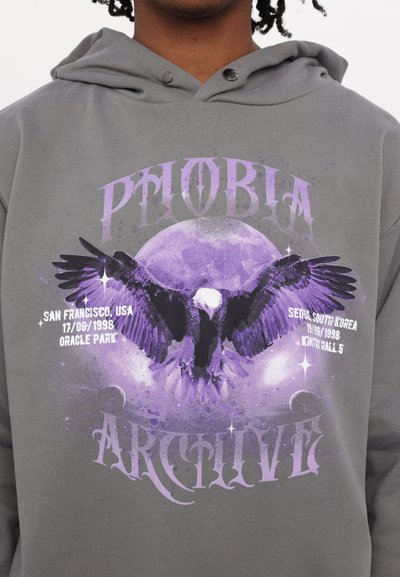 Felpa grigia con un design grafico di un'aquila con le ali spiegate sopra una luna viola. Gli elementi testuali includono "PHOBIA" e "ARCHIVE."