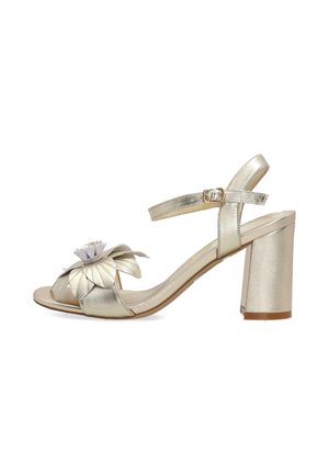 Goldene Sandale mit offenem Zehenbereich, Blockabsatz, Knöchelriemen mit Schnalle und großer mehrlagiger Blumenverzierung am Vorderriemen.