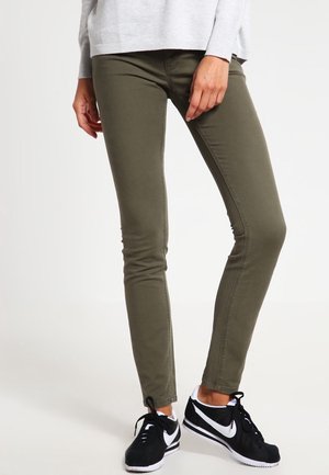 Persoon draagt olijfgroene slim-fit broek, lichtgrijze longsleeve en zwarte Nike sneakers met wit Swoosh-logo.