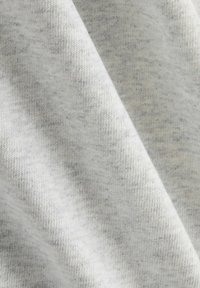 Tela gris claro con una textura suave, que presenta un sutil patrón jaspeado y una estructura de punto visible. Se observan pequeñas manchas oscuras dispersas.