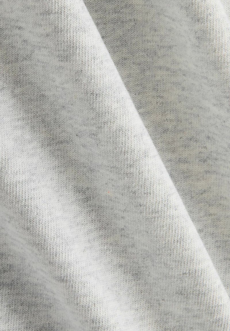 Lichtgrijze stof met een zachte textuur, voorzien van een subtiel heatherpatroon en een zichtbare breistructuur. Verspreid zijn er donkere stippen aanwezig.