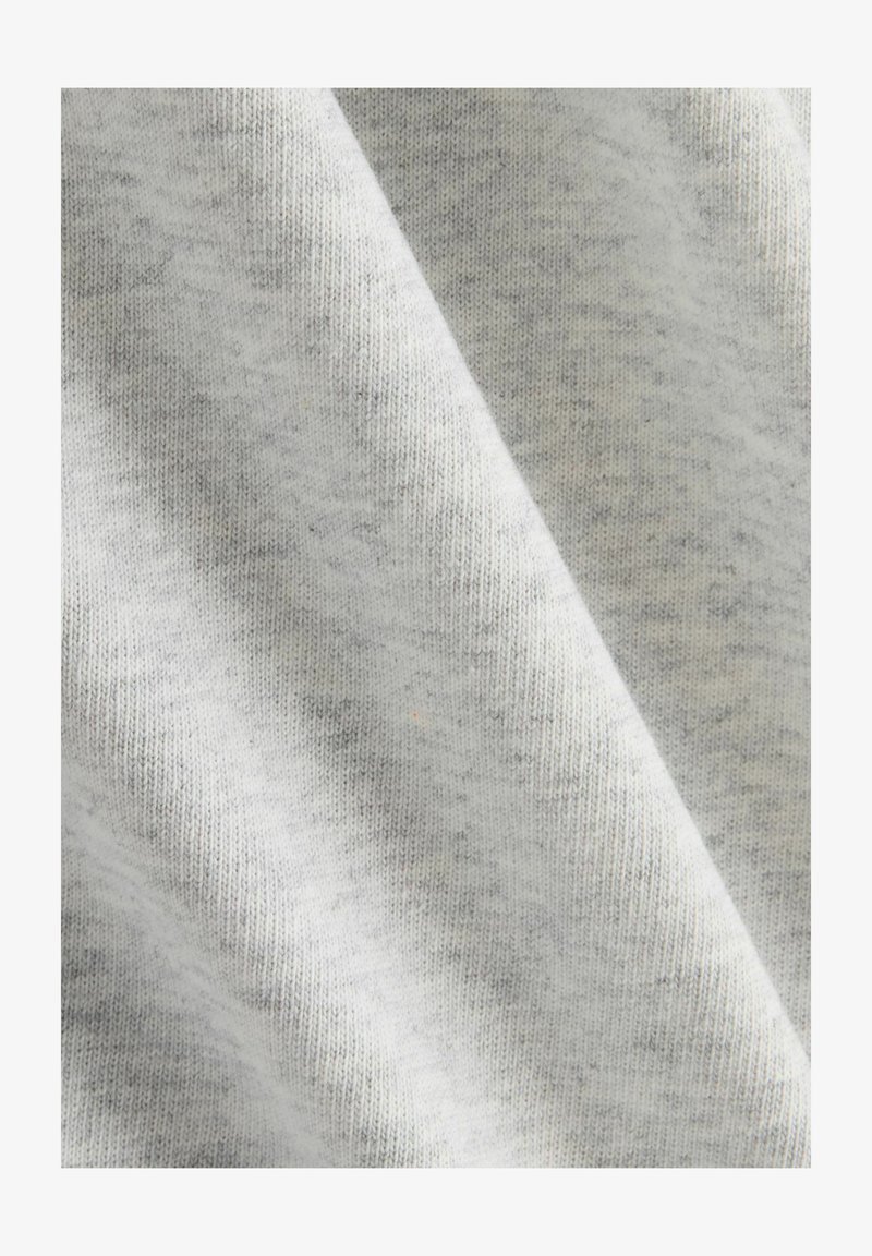 Un tissu gris clair avec une texture douce, présentant un motif chiné subtil et une structure de tricot visible. Des éclats foncés sont dispersés ici et là.