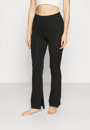 Black flared leggings made of stretchy fabric with a smooth texture. Features side slits at the hem and a flat waistband.