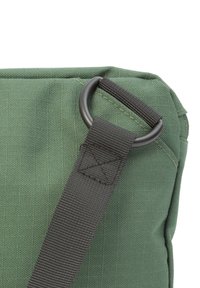 Nahaufnahme einer grünen Tasche, die einen schwarzen Riemen zeigt, der an einem Metallring befestigt ist und die Textur des Stoffes hervorhebt.