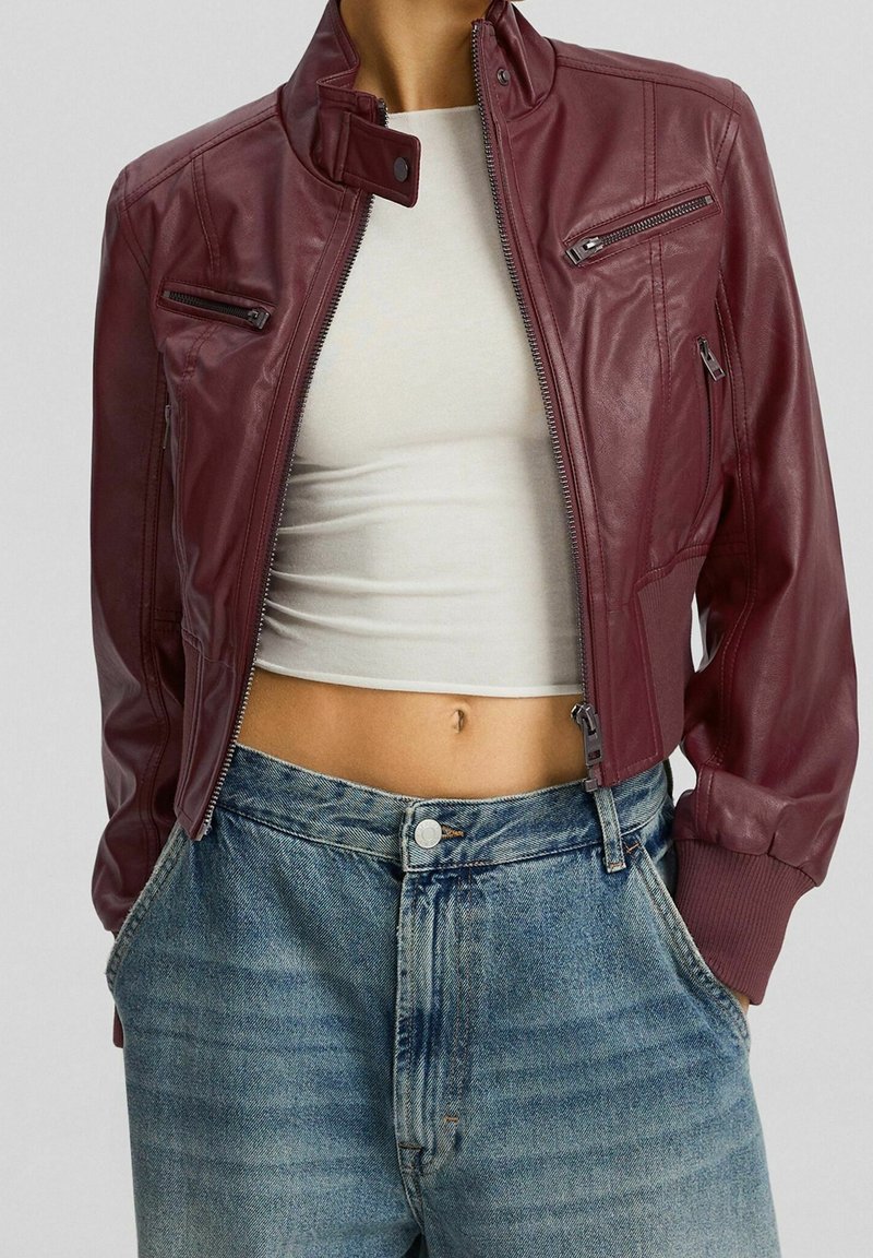 Bordeauxrode leren bomberjack met een hoge kraag, ritssluitingen op de zakken en geribbelde manchetten, gecombineerd met lichtblauwe jeans met hoge taille.