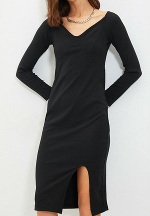 Schwarzes geripptes Kleid mit langen Ärmeln, tiefem V-Ausschnitt und seitlichem Schlitz für zusätzliche Details. Glatte Textur, figurbetonte Silhouette.