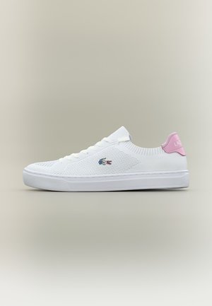 Baskets basses blanches avec texture tricotée, lacets blancs, languette rose au talon et petit logo crocodile Lacoste brodé sur le côté.