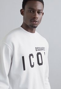 White sweatshirt made of smooth cotton, featuring bold black "ICON" text and "DSQUARED2" branding on the chest; crew neck design.
