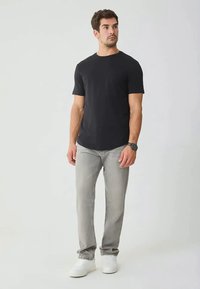 Μαύρο μπλουζάκι με κοντά μανίκια, συνδυασμένο με ανοιχτό γκρι τζιν παντελόνι. Το μοντέλο φοράει λευκά αθλητικά παπούτσια και ρολόι. Απλός, εφαρμοστός σχεδιασμός με στρογγυλή λαιμόκοψη.