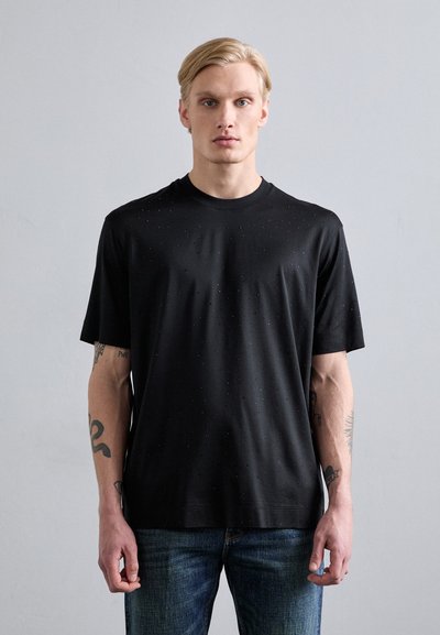 T-shirt nero a maniche corte con collo tondo, caratterizzato da una sottile texture a pois. Abbinato a jeans in denim blu.