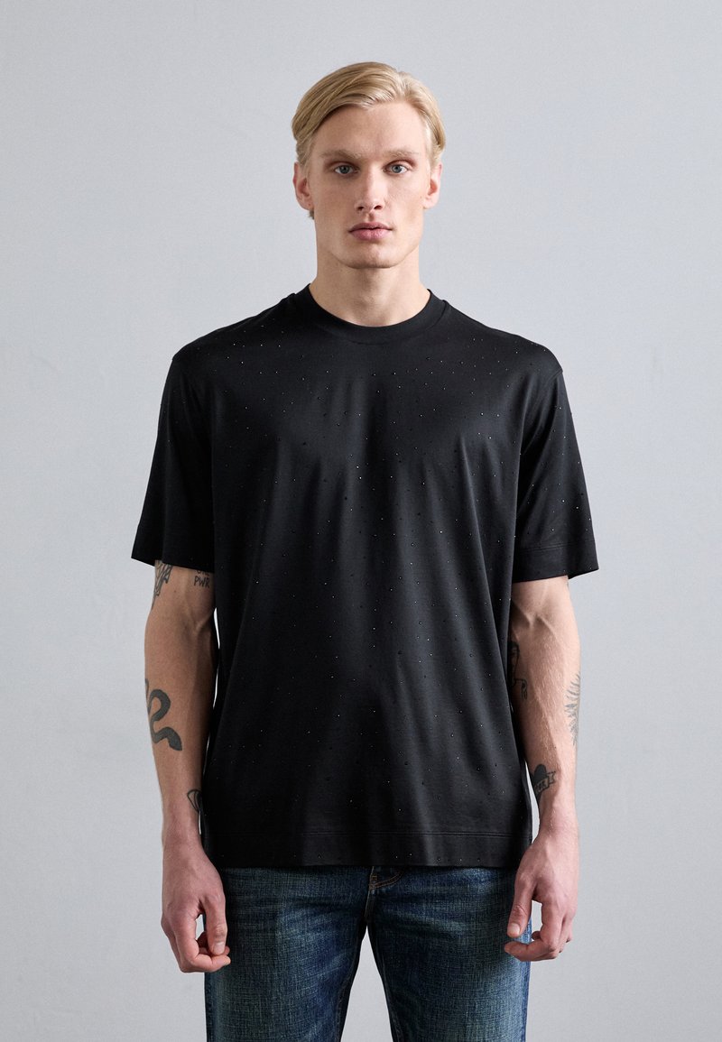 Svart kortermet T-skjorte med rund hals, med en subtil prikkete tekstur. Sammen med blå denimjeans.