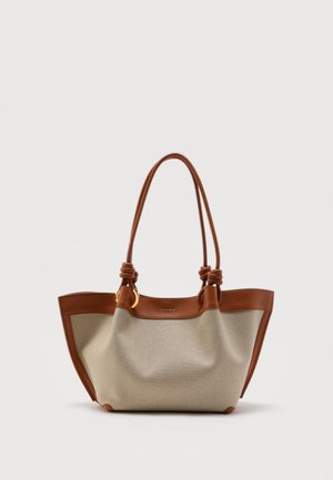 Borsa tote in tela beige con rifiniture e manici in pelle marrone, caratterizzata da dettagli annodati sui manici e decorazioni a forma di anello dorato.