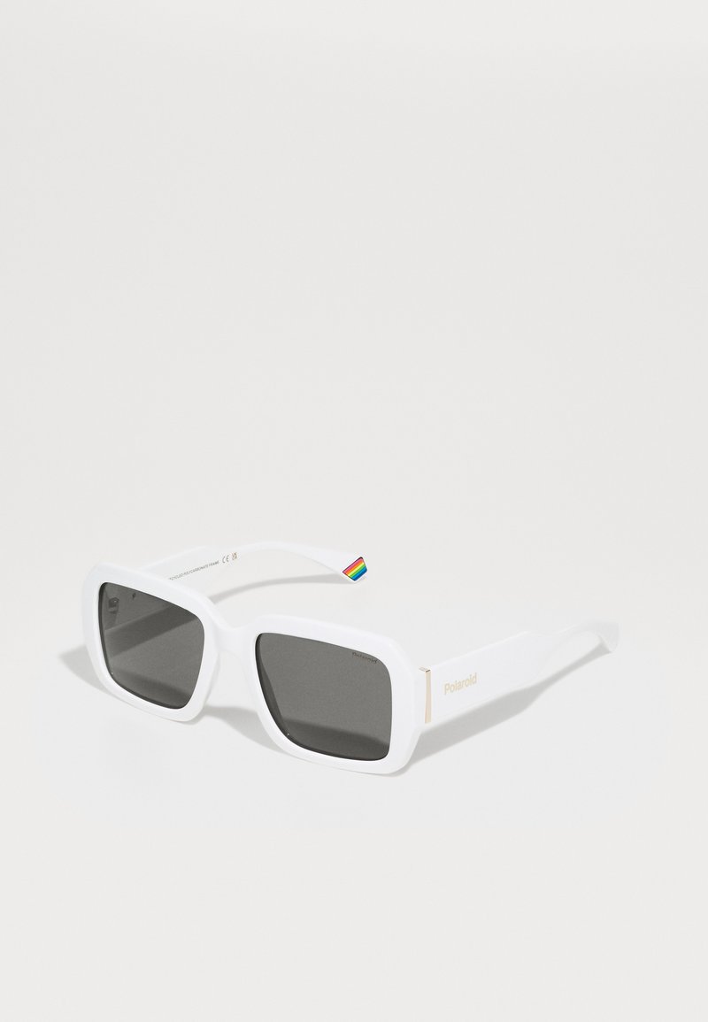 Lunettes de soleil rectangulaires blanches avec des verres gris. Présente un logo Polaroid doré et un accent arc-en-ciel sur la branche. Texture en plastique lisse.